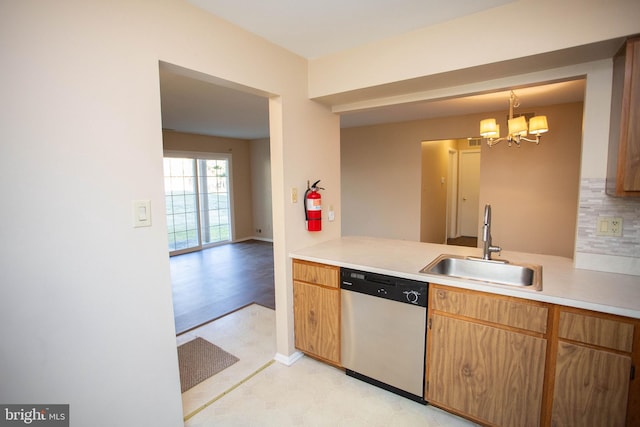 kitchen with a notable chandelier, a sink, light countertops, stainless steel dishwasher, and backsplash