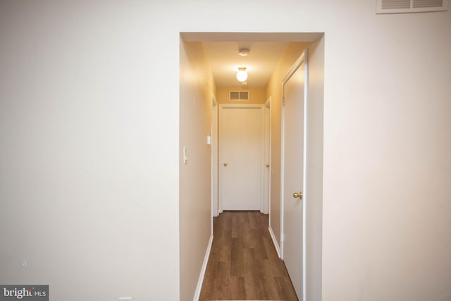 corridor with baseboards, visible vents, and wood finished floors