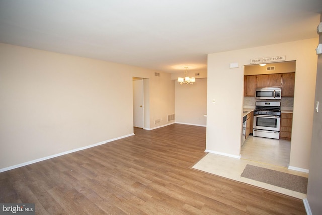 unfurnished living room with an inviting chandelier, light wood-style flooring, visible vents, and baseboards