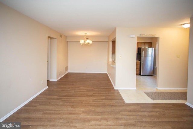 unfurnished room featuring light wood-style flooring, baseboards, and an inviting chandelier