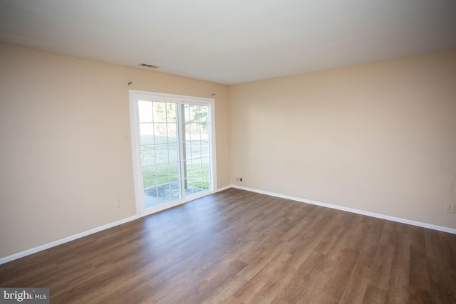 unfurnished room featuring dark wood-type flooring, visible vents, and baseboards