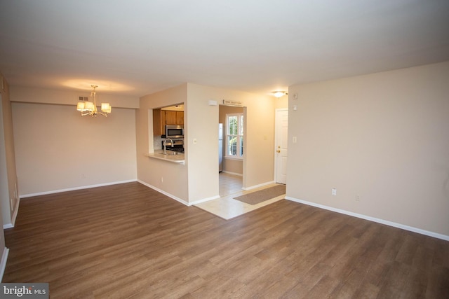 unfurnished living room featuring a sink, an inviting chandelier, baseboards, and wood finished floors