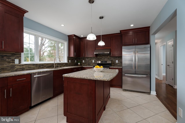 kitchen featuring light tile patterned floors, appliances with stainless steel finishes, light stone countertops, under cabinet range hood, and a sink