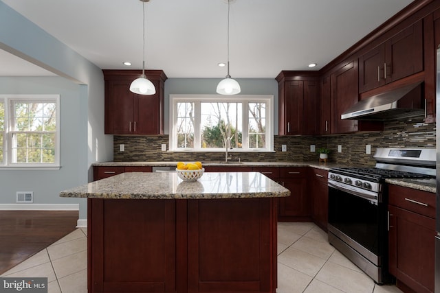 kitchen with light tile patterned floors, visible vents, light stone countertops, under cabinet range hood, and stainless steel range with gas cooktop