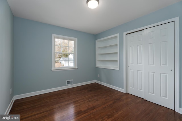 unfurnished bedroom with a closet, visible vents, dark wood finished floors, and baseboards