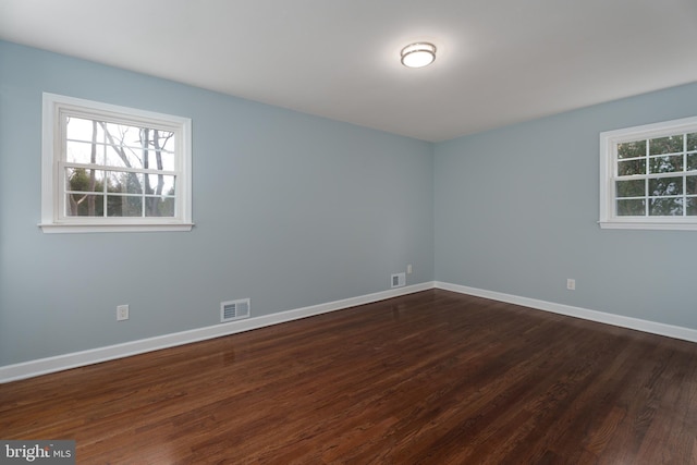 empty room with plenty of natural light, visible vents, dark wood-style flooring, and baseboards