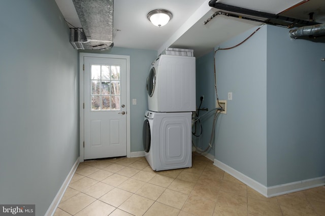 clothes washing area featuring laundry area, light tile patterned flooring, stacked washer and clothes dryer, and baseboards