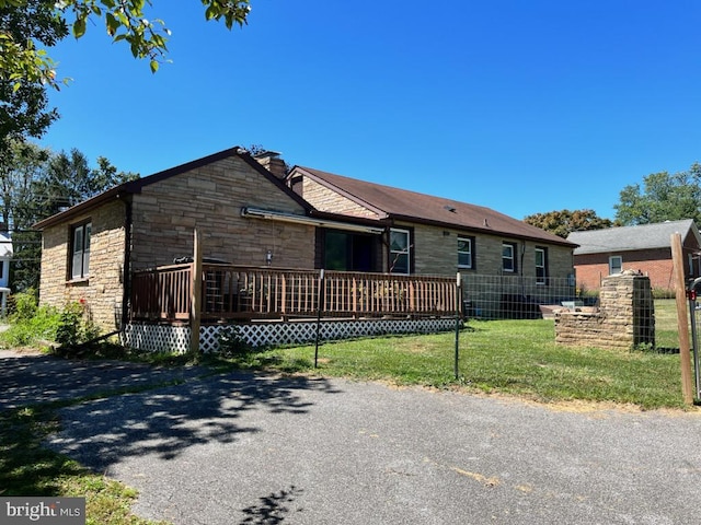 view of front of property featuring stone siding, a chimney, fence, a wooden deck, and a front lawn