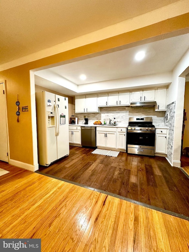 kitchen featuring appliances with stainless steel finishes, light countertops, under cabinet range hood, and dark wood-type flooring