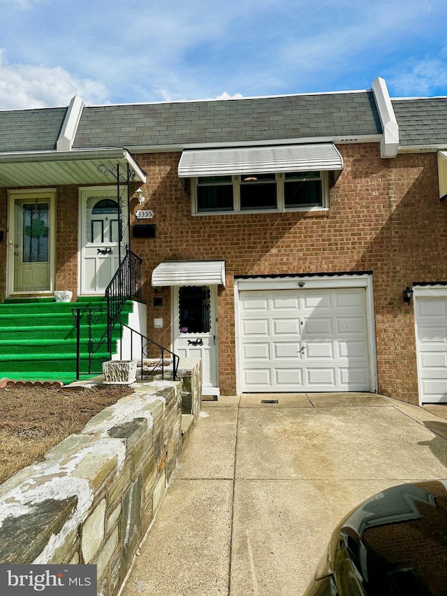 multi unit property featuring brick siding, mansard roof, a shingled roof, an attached garage, and driveway