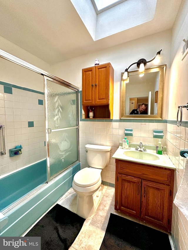 full bath with toilet, bath / shower combo with glass door, a skylight, vanity, and tile walls