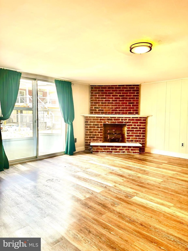 unfurnished living room featuring a brick fireplace, baseboards, and wood finished floors