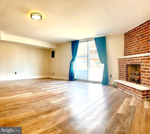 unfurnished living room featuring a brick fireplace, baseboards, and wood finished floors