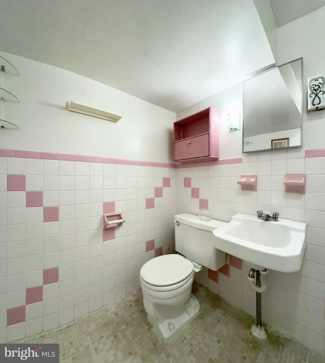 bathroom with toilet, a wainscoted wall, tile walls, and a sink