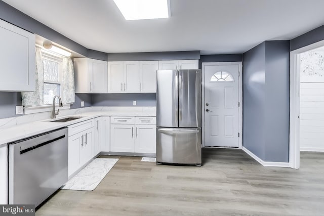 kitchen with baseboards, appliances with stainless steel finishes, light wood-style floors, white cabinetry, and a sink