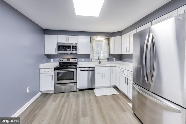 kitchen featuring stainless steel appliances, light wood-style floors, white cabinets, a sink, and baseboards