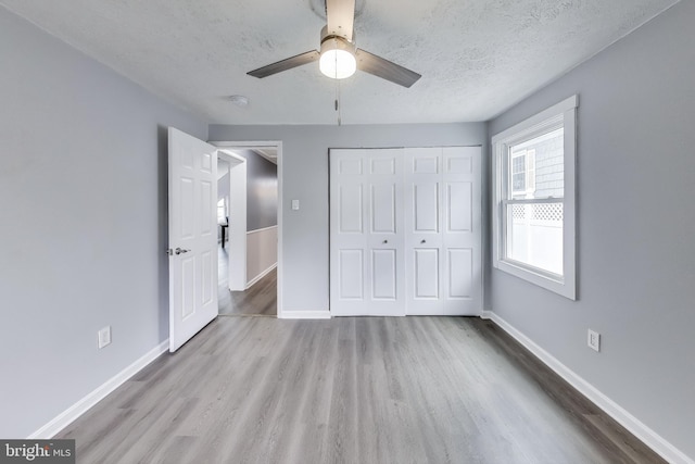 unfurnished bedroom featuring a closet, a textured ceiling, baseboards, and wood finished floors