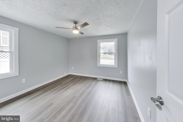 unfurnished room with baseboards, visible vents, ceiling fan, wood finished floors, and a textured ceiling