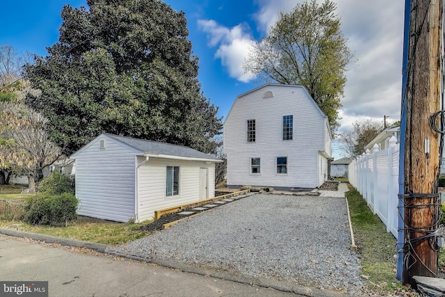 back of property featuring gravel driveway, fence, and an outdoor structure