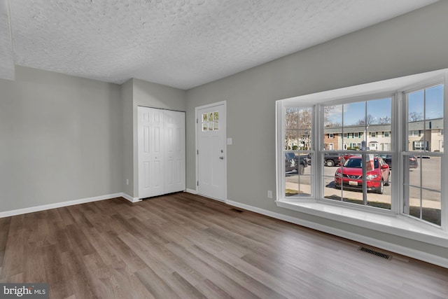 interior space featuring visible vents, a textured ceiling, baseboards, and wood finished floors