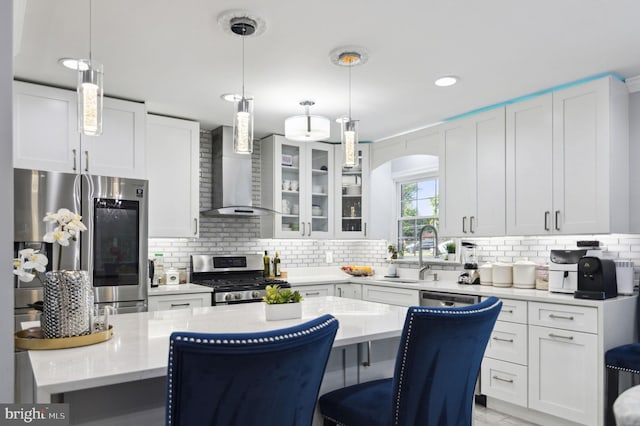 kitchen featuring stainless steel appliances, tasteful backsplash, light countertops, a sink, and wall chimney range hood