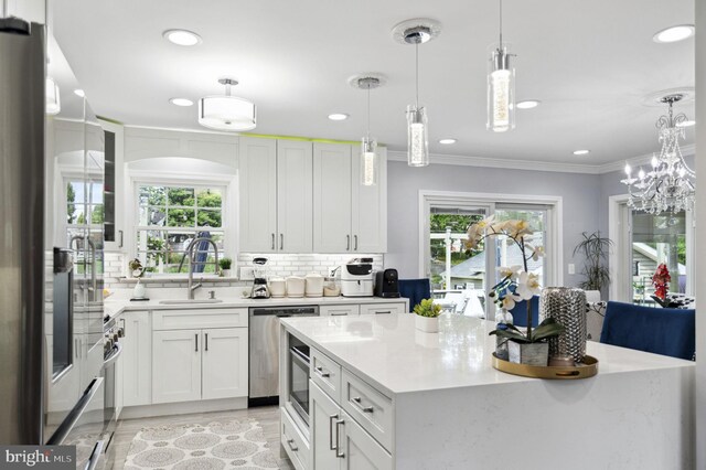 kitchen featuring crown molding, backsplash, appliances with stainless steel finishes, a healthy amount of sunlight, and a sink