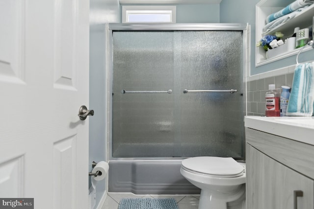 bathroom featuring tile walls, bath / shower combo with glass door, toilet, vanity, and tile patterned flooring