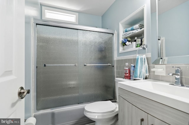 bathroom with enclosed tub / shower combo, vanity, toilet, and tile walls