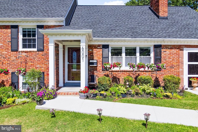 entrance to property with roof with shingles, a chimney, and brick siding