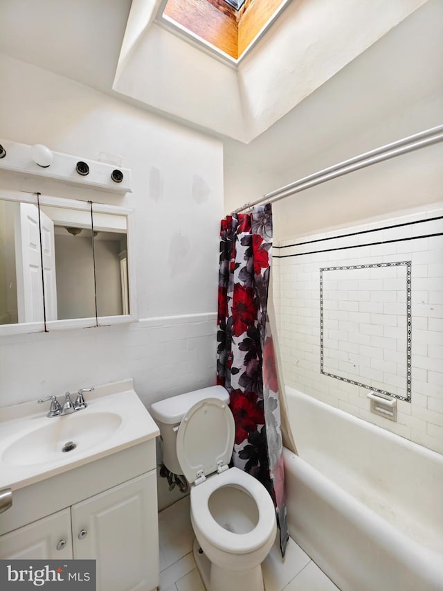 bathroom featuring a skylight, wainscoting, toilet, vanity, and tile walls