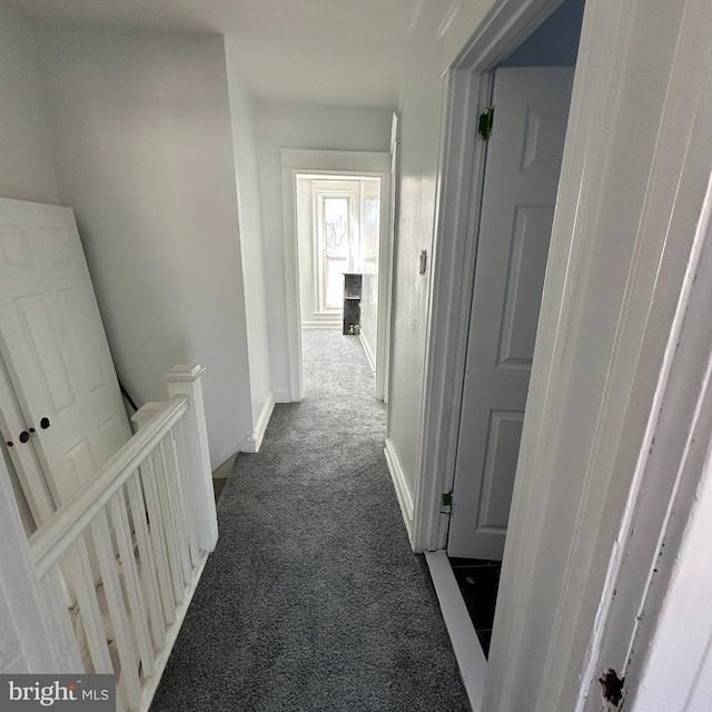 hall with dark colored carpet, baseboards, and an upstairs landing