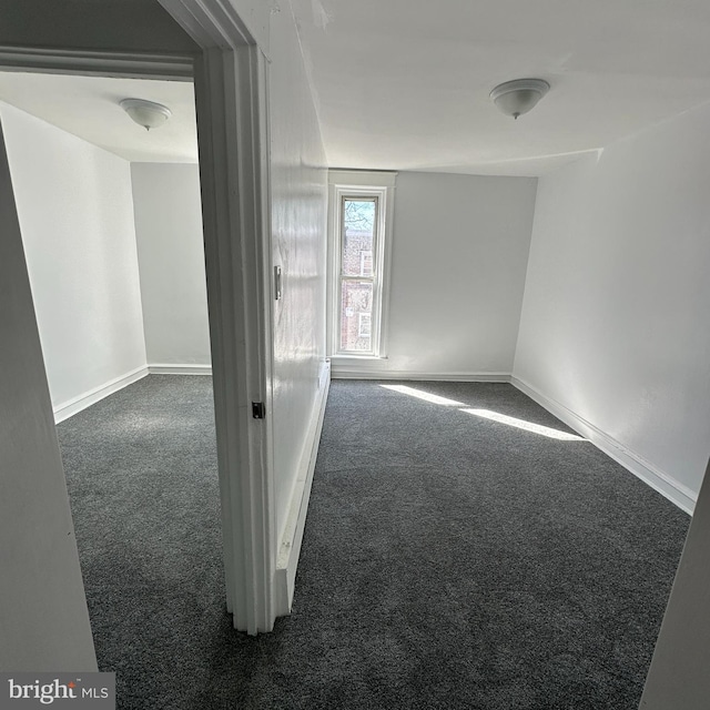 spare room featuring baseboards and dark carpet