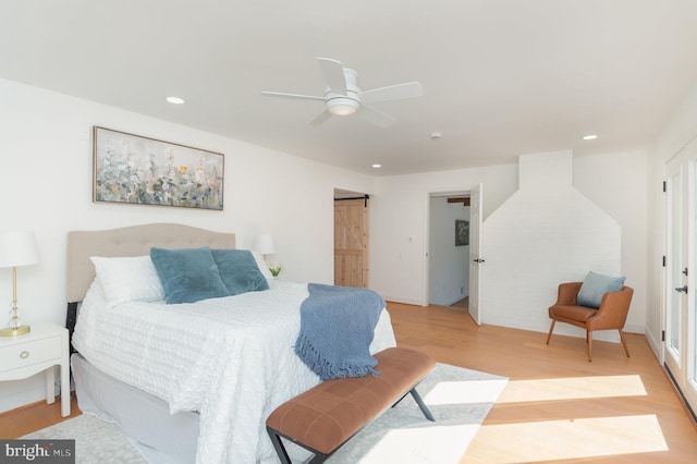 bedroom featuring light wood finished floors, ceiling fan, a barn door, and recessed lighting