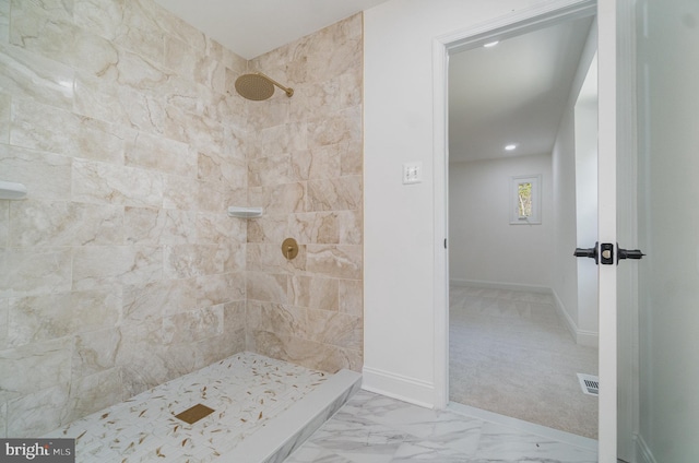 bathroom featuring marble finish floor, tiled shower, visible vents, and baseboards