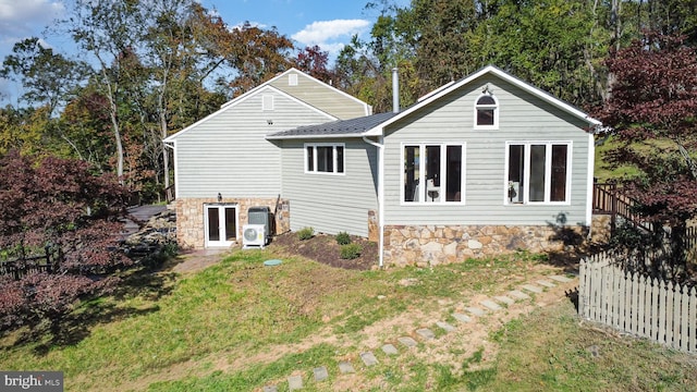 back of house featuring stone siding, french doors, a lawn, and fence