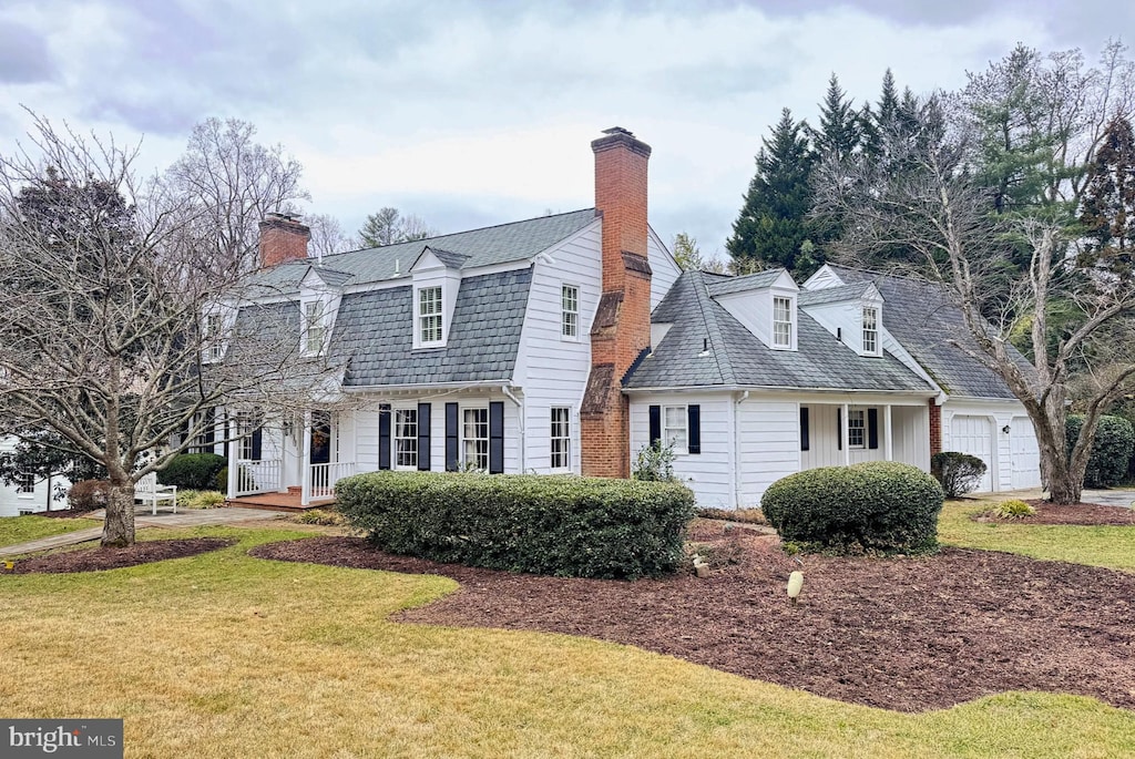 colonial inspired home with a garage, a chimney, a gambrel roof, and a front yard