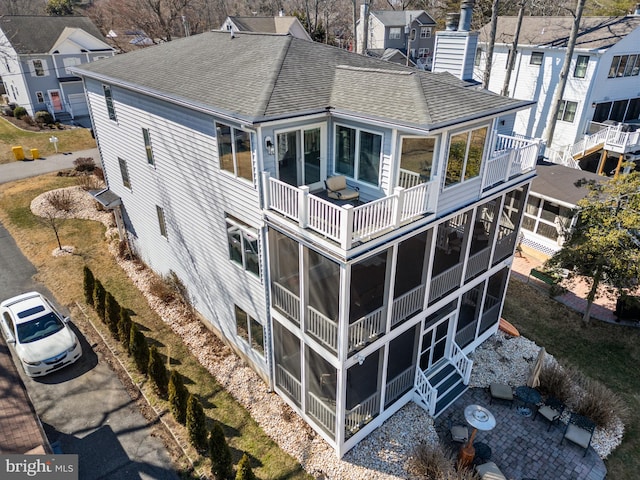 back of house with a balcony, a sunroom, a shingled roof, and a chimney