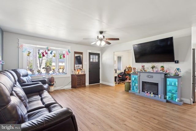 living room featuring a ceiling fan, a fireplace, baseboards, and wood finished floors