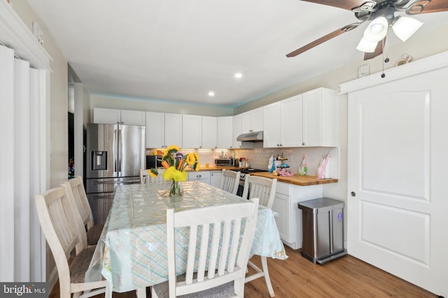 kitchen with light wood finished floors, stainless steel fridge with ice dispenser, stove, under cabinet range hood, and backsplash