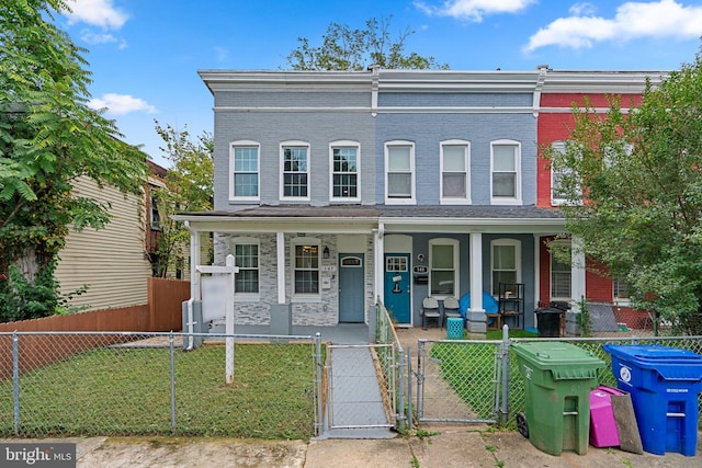 view of property with covered porch, a fenced front yard, a gate, and brick siding