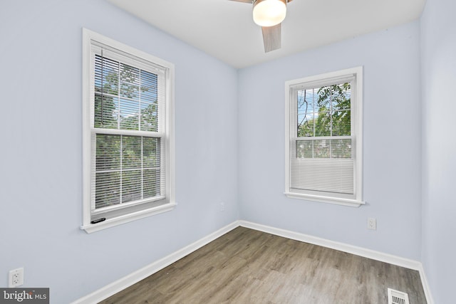 empty room featuring a healthy amount of sunlight, baseboards, visible vents, and wood finished floors