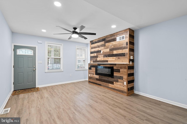 foyer entrance with a fireplace, wood finished floors, a ceiling fan, visible vents, and baseboards