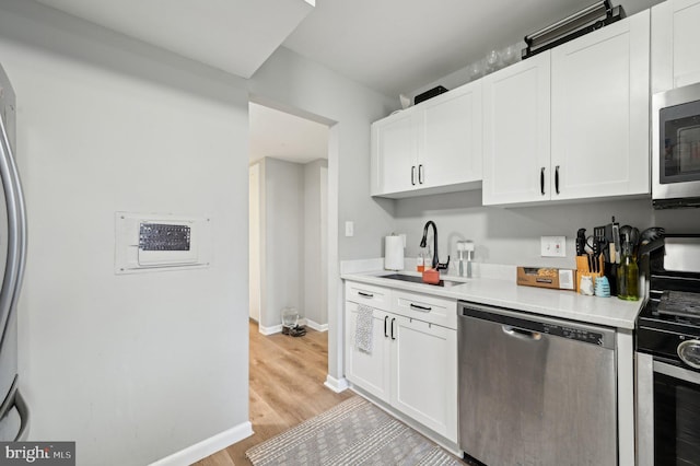 kitchen with baseboards, appliances with stainless steel finishes, light countertops, white cabinetry, and a sink