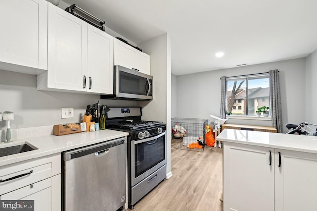 kitchen with appliances with stainless steel finishes, light wood-type flooring, white cabinets, and a sink