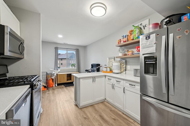 kitchen with stainless steel appliances, light wood finished floors, a peninsula, and light countertops