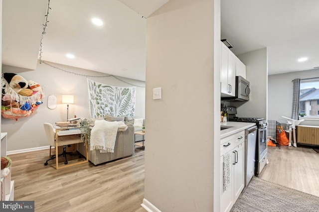 kitchen featuring stainless steel appliances, light wood-type flooring, radiator, and white cabinets