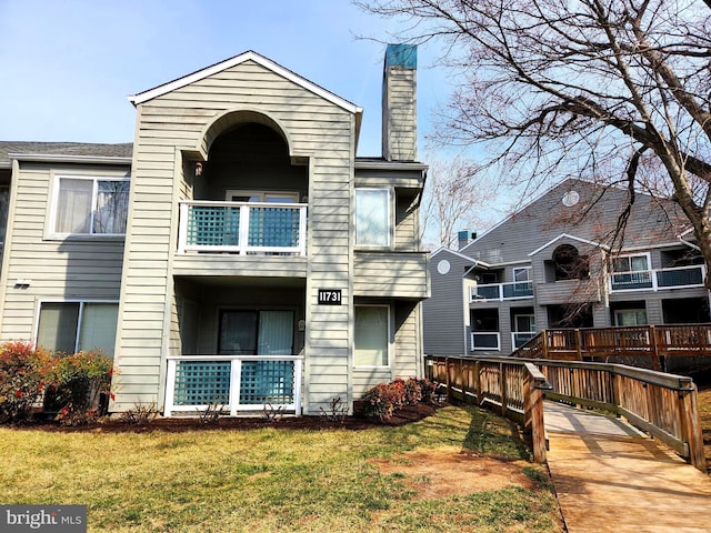 rear view of house with a balcony, a chimney, and a lawn