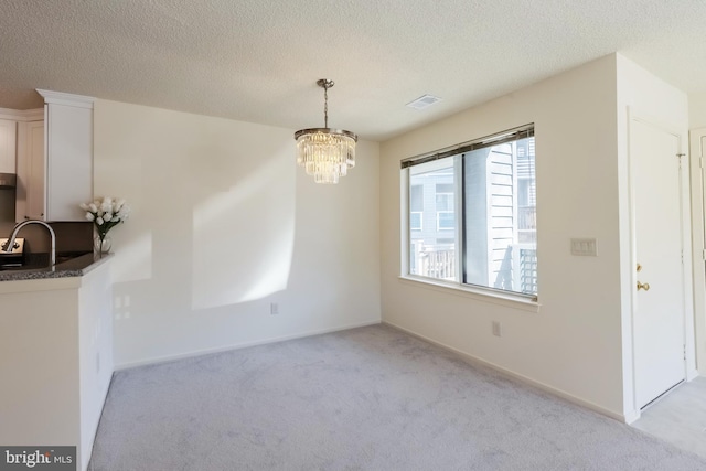 unfurnished dining area with visible vents, a chandelier, a textured ceiling, and light colored carpet