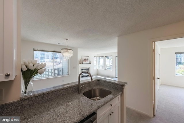 kitchen with white cabinets, light colored carpet, open floor plan, dark stone countertops, and a sink