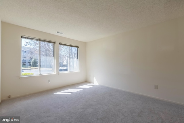 unfurnished room with a textured ceiling, carpet floors, and visible vents